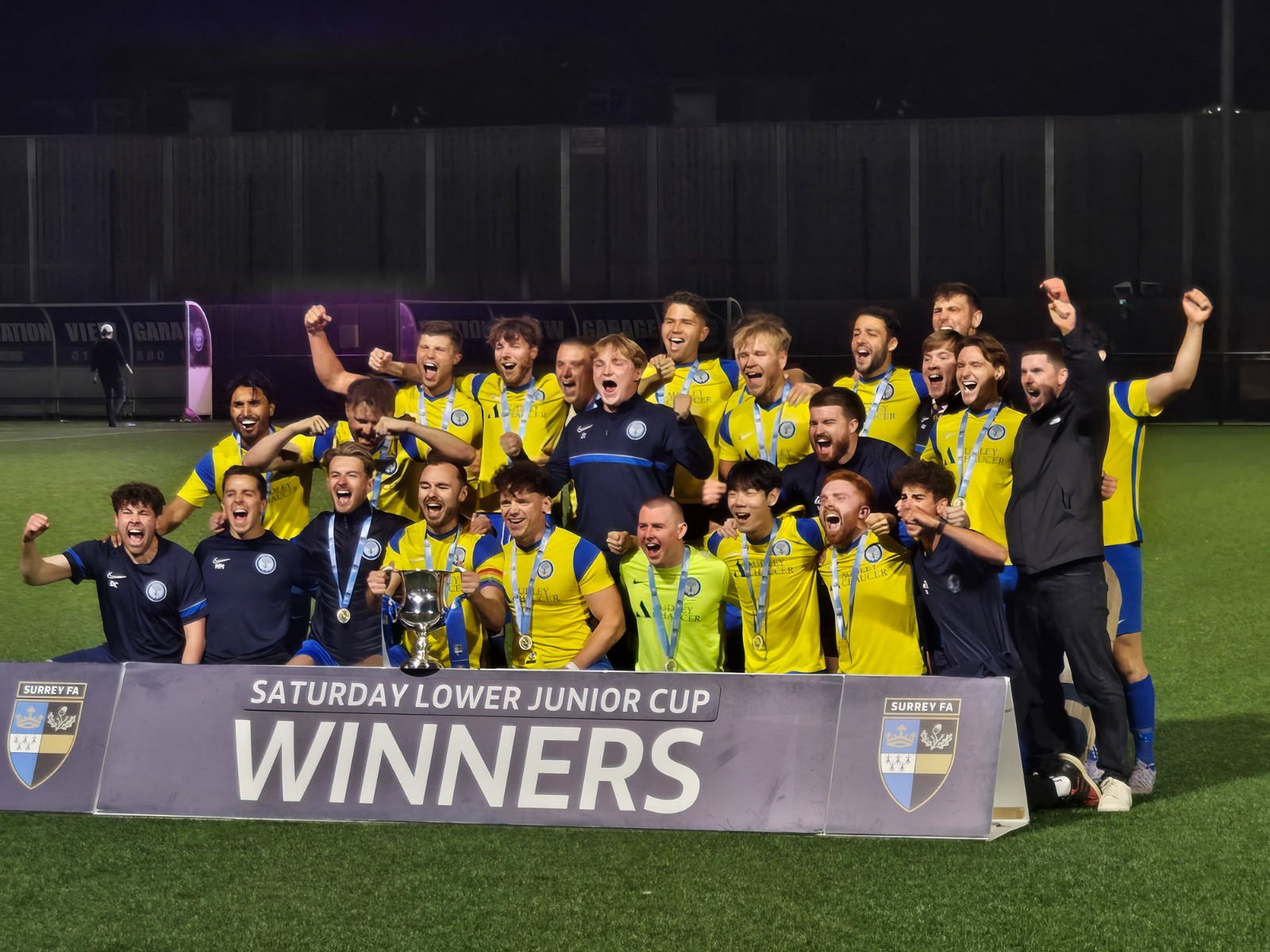 New Elm FC celebrating with the cup behind the winners board
